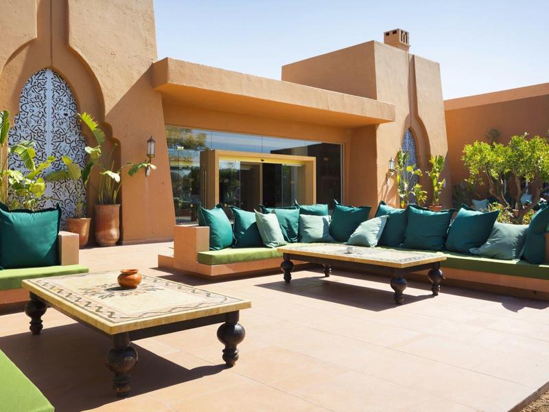 Bright terrace with comfortable sofas and decorative plants in front of a building.