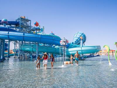 Des enfants et des adultes profitent d'un parc aquatique avec de grands toboggans bleus sous un ciel clair.