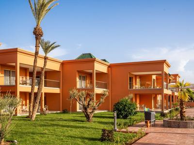 Bâtiment d'hôtel orange avec balcons et jardin vert bien entretenu sous un ciel clair.