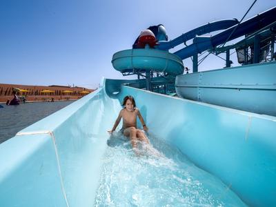 Un enfant glisse sur un toboggan aquatique bleu clair dans un parc aquatique par une journée ensoleillée.