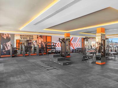Grande salle de sport avec équipements et accents orange dans un hôtel.