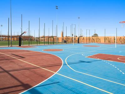 Terrain de basket vide avec sol bleu et rouge et clôture en treillis sous ciel clair.