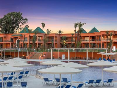 Complexe hôtelier moderne avec piscine, parasols et chaises longues au coucher du soleil.
