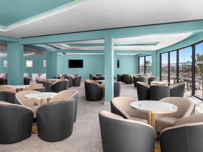 Salon d'hôtel moderne avec fauteuils confortables et grandes fenêtres offrant une vue sur la mer.