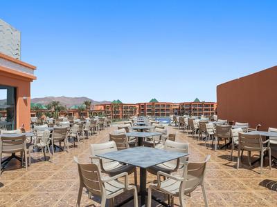 Grande terrasse d'hôtel avec de nombreuses tables et chaises sous un ciel bleu clair.
