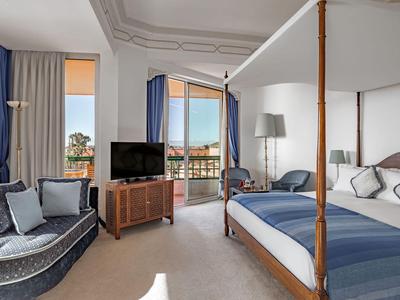 Elegantes Hotelzimmer mit Himmelbett, Sofa und großen Fenstern mit Blick auf die Stadt.