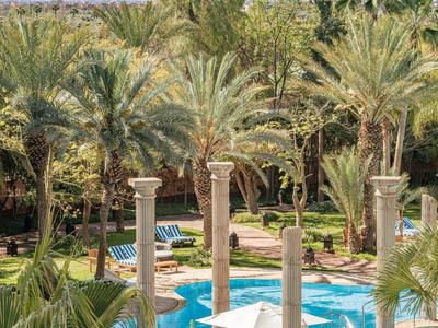 Pool in runder Anlage mit Säulen, umgeben von Palmen und grüner Vegetation bei klarem Himmel.