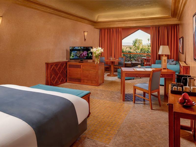 Chambre d'hôtel confortable avec lit, coin salon, TV et vue sur terrasse et jardin.