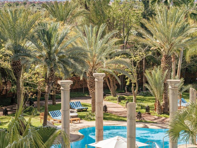 Espace piscine avec de grands palmiers et des colonnes anciennes entourées de verdure luxuriante.