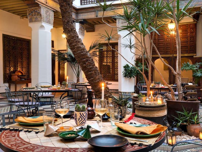 Elegant restaurant with round table set and tropical plants in historic hall.