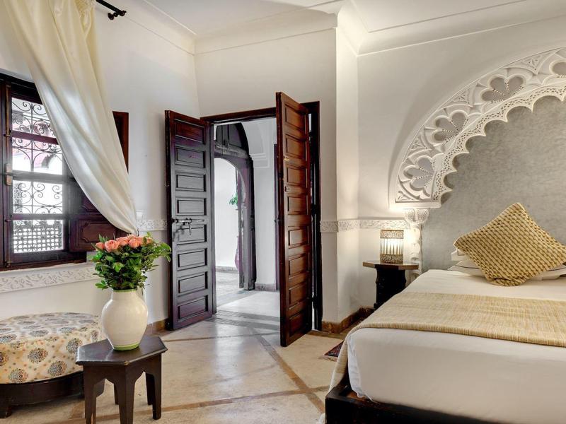 Brightly furnished bedroom with large bed, ornate walls, and open window.