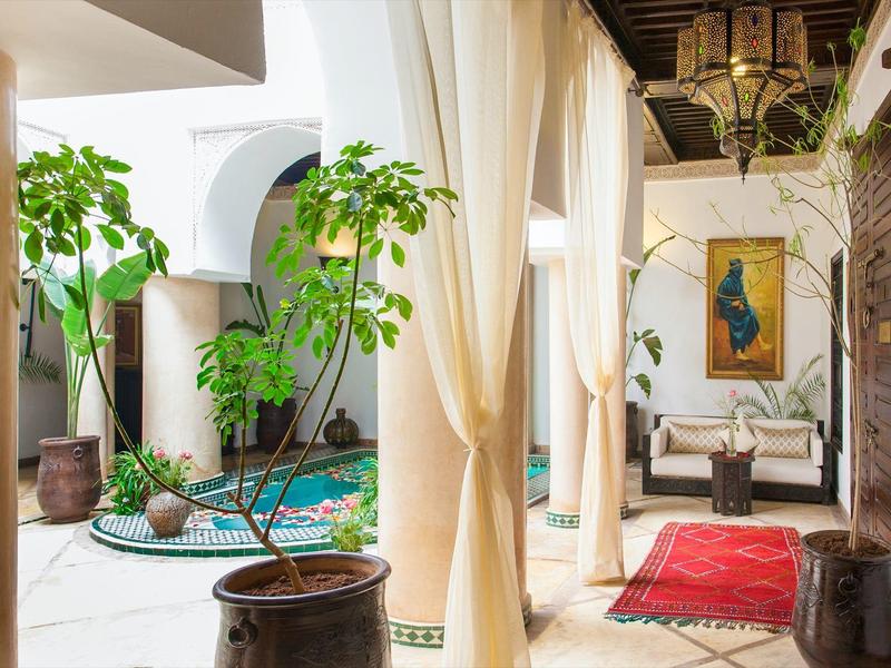 Bright hotel lounge with tall columns, curtains, plants, and cozy seating areas.