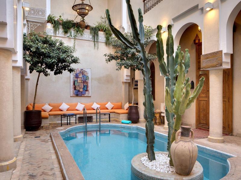 Courtyard with small pool, cactus plants, and seating area with orange cushions.