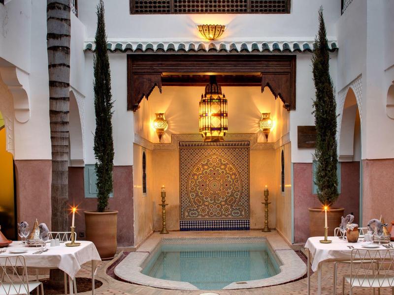 Elegant courtyard with pool, dining tables, and decorative lighting in Moroccan style.