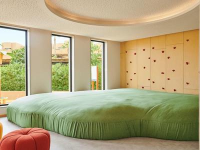 Modern hotel room with green, organically shaped bed and floor-to-ceiling windows.