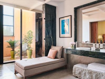 Modern hotel room with chaise lounge, large mirror, and balcony with plants.