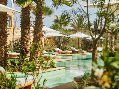 Hotelpool an einem sonnigen Tag, umgeben von Palmen und Liegestühlen mit Sonnenschirmen.