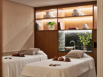 Two massage tables in a calm spa room with warm lighting and plants.