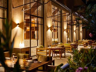 Abendliche Terrasse eines Restaurants mit beleuchteten Tischen und Stühlen neben einer Glasfassade.