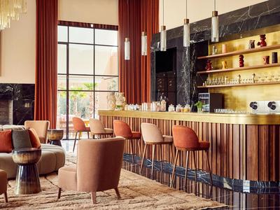 Moderner Hotelbarbereich mit Ledersesseln und hohen Barhockern vor einem goldenen Tresen.