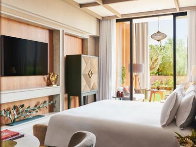 Modern hotel room with large bed, TV, closet, and balcony overlooking greenery.