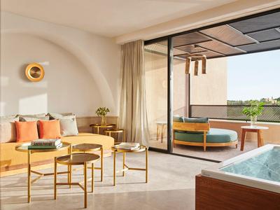 Modernes Hotelzimmer mit Balkon, Dusche im Zimmer und Sitzbereich mit Gelb- und Orangetönen.