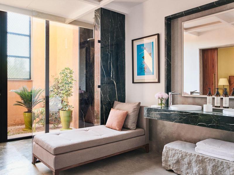 Modern hotel room with chaise lounge, large mirror, and balcony with plants.