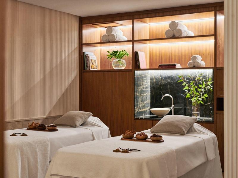Two massage tables in a calm spa room with warm lighting and plants.