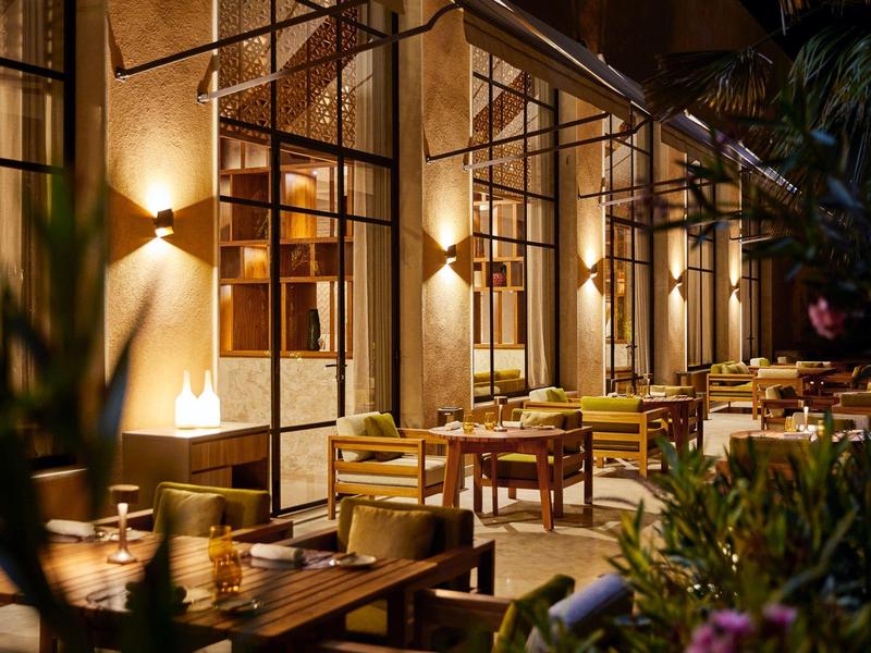 Cozy illuminated restaurant terrace with wooden chairs and tables at dusk.