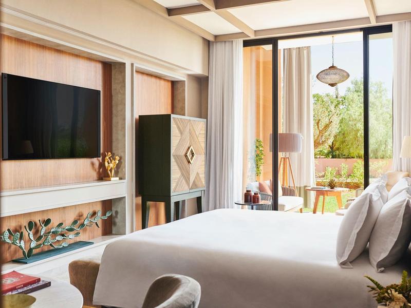 Modern hotel room with large bed, TV, closet, and balcony overlooking greenery.