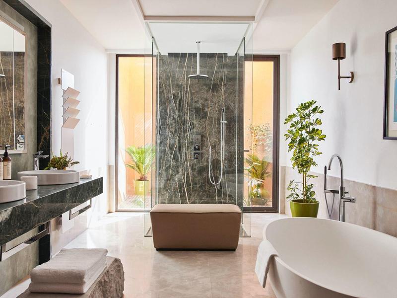 Bright bathroom with freestanding bathtub and large shower in front of floor-to-ceiling windows.