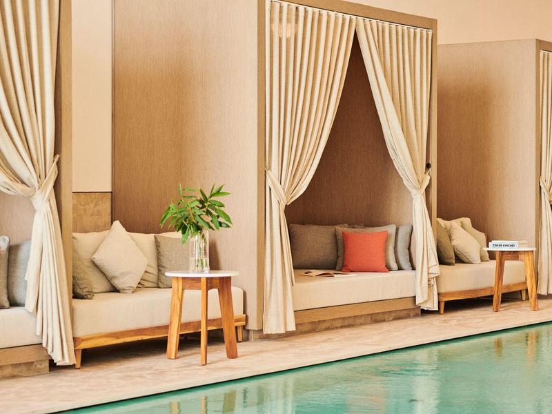 Cozy lounge nooks with curtains beside a tranquil pool in a hotel setting.