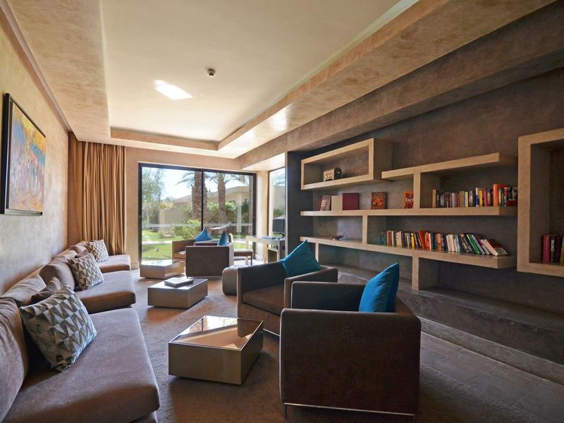 Salon moderne avec étagères, canapés et grandes fenêtres donnant sur la verdure.