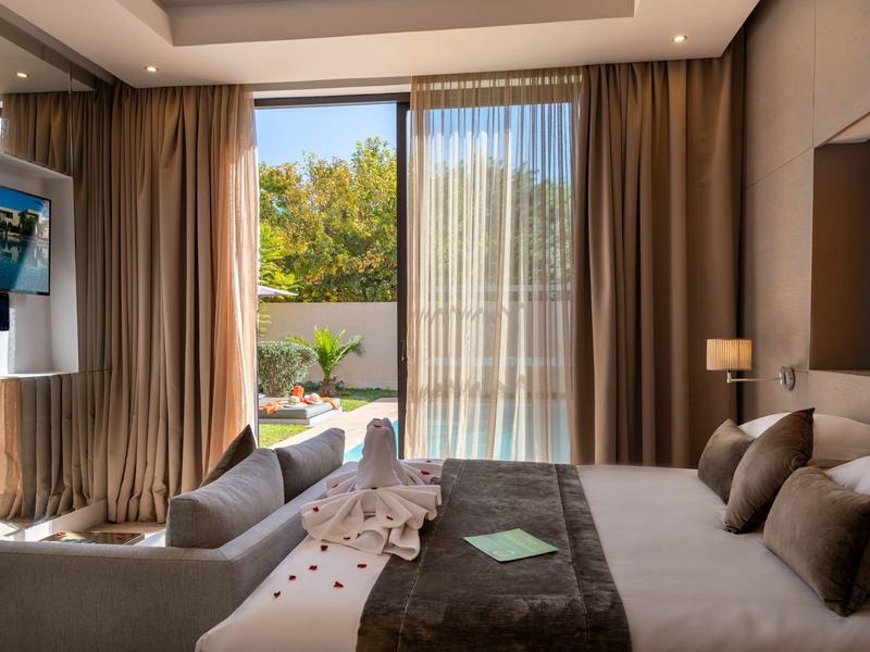 Chambre d'hôtel moderne avec grand lit, canapé, rideaux et vue sur terrasse jardin