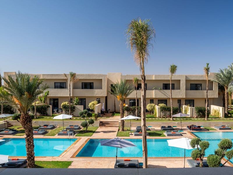 Complexe hôtelier moderne avec deux piscines et des palmiers sous un ciel dégagé