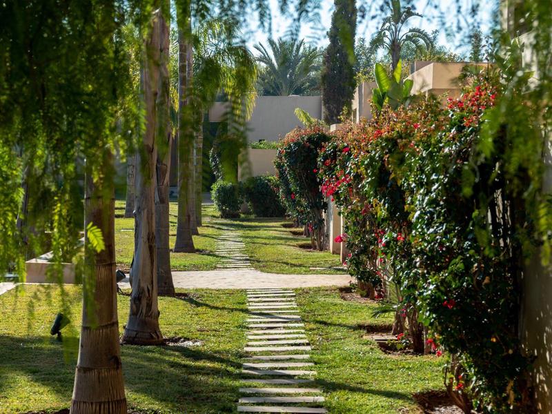 Chemin avec dalles en pierre entre des palmiers et des arbustes en fleurs dans un jardin d'hôtel.