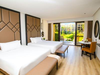 Habitación de hotel con dos camas dobles, suelo de madera y vista al jardín a través de grandes ventanas