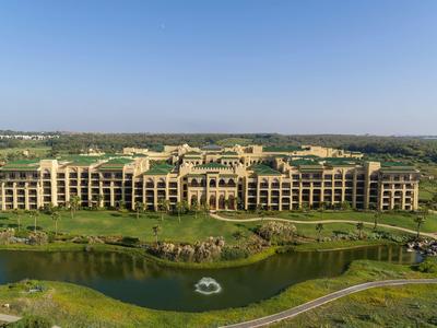Gran hotel de varios pisos rodeado de paisajes verdes y un estanque.