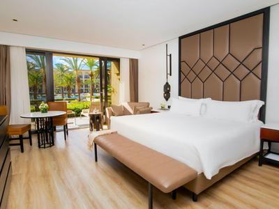 Habitación de hotel luminosa con cama grande, decoración moderna y vista a palmeras tropicales.