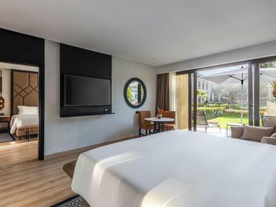 Habitación de hotel luminosa con cama doble, televisor, escritorio y vista al jardín a través de ventana de vidrio.