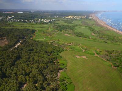 Paisaje con campos verdes, zona boscosa y línea costera con vista al mar en el fondo.