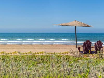 Dos sillas y una sombrilla en una playa tranquila con vista al mar bajo un cielo despejado.