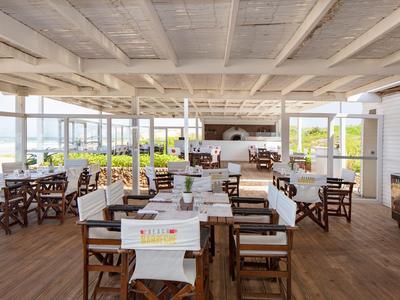 Restaurante luminoso con suelos de madera, mesas blancas y vista al mar.