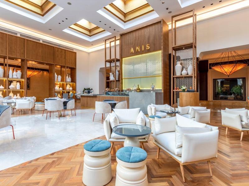 Salón elegante de hotel con cómodos sillones blancos, taburetes azules y blancos, y suelo de madera cálido.