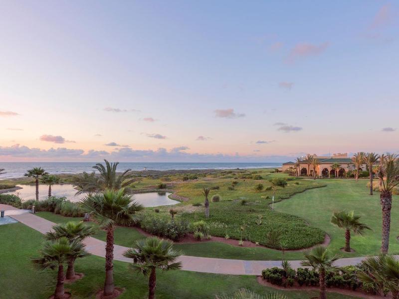 Vista de jardines cuidadosos con palmeras y campo de golf bajo un cielo despejado al atardecer.