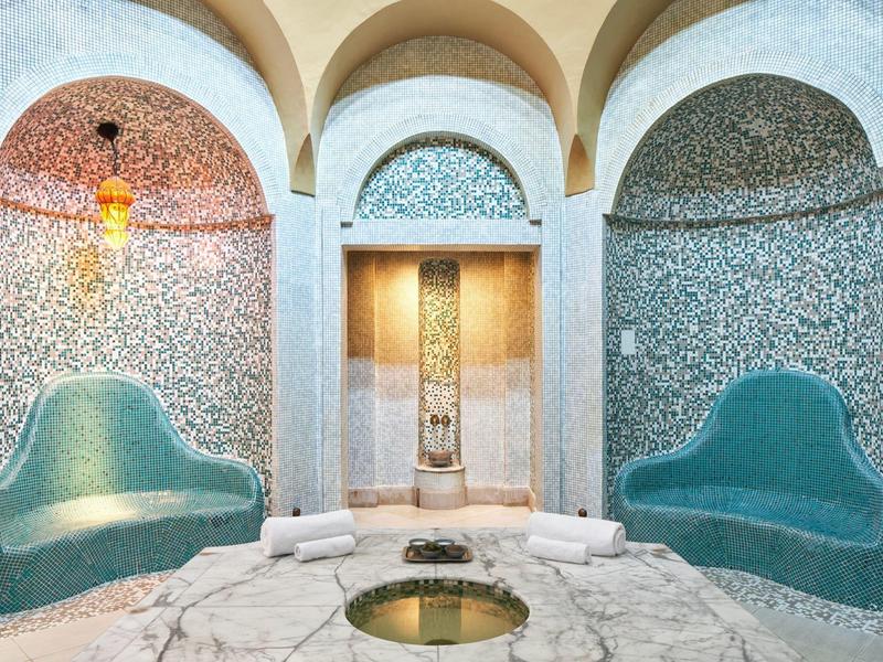 Área de spa elegante con azulejos de mosaico, dos sofás y un estanque redondo en el centro.