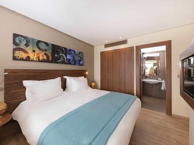 Chambre d'hôtel moderne avec lit double, jeté bleu et vue sur la salle de bain.