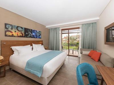 Chambre d'hôtel lumineuse avec lit double, coin salon et balcon donnant sur la verdure.