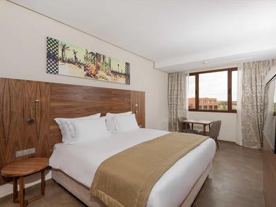 Chambre d'hôtel lumineuse avec lit double, meubles en bois et fenêtre avec vue extérieure.