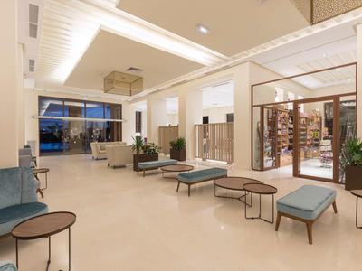 Prostorná, moderní hotelová hala s posezením a velkými okny, světlé osvětlení.